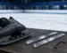 Eishockey-Schlittschuh mit leerem Halter neben zwei neuen Ersatzkufen auf der Bank an der Eisbahn – Kufen für Schlittschuhe